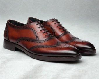 May include: A pair of brown leather dress shoes with brogue detailing. The shoes have a classic wingtip design with decorative perforations and dark brown laces. The leather has a polished finish and a subtle gradient of color.