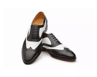 May include: Black and white leather oxford shoes with brogue detailing. The shoes have a lace-up closure and a pointed toe.