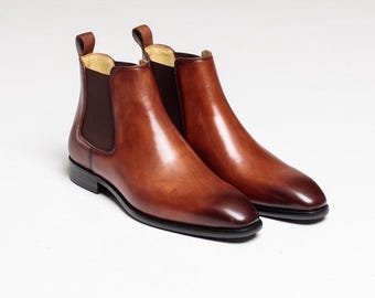 May include: A pair of brown leather Chelsea boots with elastic side panels and pull tabs. The boots have a polished finish and black soles. The footwear is displayed on a white background.