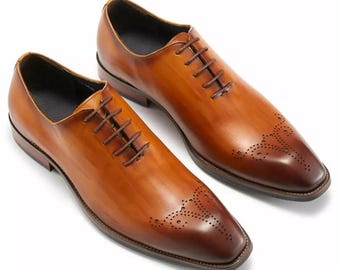 May include: A pair of brown leather dress shoes with a polished finish. The shoes have a classic Oxford design with a lace-up closure and decorative perforations on the toe. The shoes are a warm brown color.