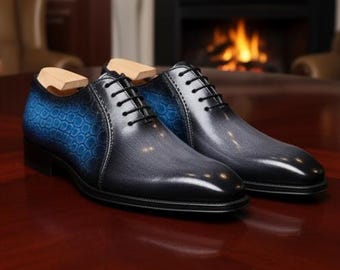 May include: A pair of men's dress shoes with a gradient design. The shoes transition from black to gray, with a blue textured pattern on the heel. Black laces and wooden shoe trees are visible.
