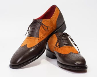 May include: A pair of brown and orange leather wingtip dress shoes. The shoes feature a perforated design on the toe and a suede panel. The laces are brown, and the interior is red. The shoes are displayed on a white background.