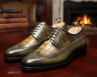 May include: A pair of olive green and tan leather dress shoes with a crocodile pattern. The shoes have a classic lace-up design and are displayed on a dark wooden surface. Wooden shoe trees are inserted inside the shoes.