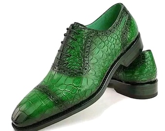 May include: A pair of green leather dress shoes with a textured, crocodile-like pattern. The shoes have a classic Oxford design with black laces and a dark sole. The shoes are displayed on a white background.