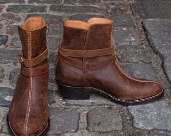 May include: A pair of brown leather ankle boots with a distressed finish. The boots feature a pointed toe, a low heel, and a strap with a buckle around the ankle. White stitching accents the seams.
