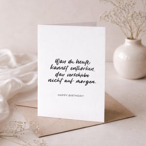 May include: A white greeting card with black script that reads "Was du heute kannst entkorken, das verschiebe nicht auf morgen." and "HAPPY BIRTHDAY!". The card is on a brown envelope.