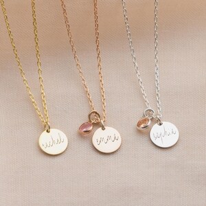 May include: Four delicate necklaces in gold, rose gold, and silver. Each necklace features a thin chain and a small, round pendant with a name engraved on it. Some pendants have a small, pink gemstone charm.