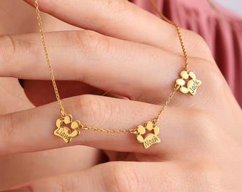 May include: A gold-colored necklace featuring paw-shaped pendants, each inscribed with a name. The necklace is held up, showcasing the delicate chain and the personalized details on the pendants. The names are Liam, Noah, and Jack.