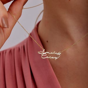 Può includere: Collana in oro con due nomi, "Amelia" e "Casey", scritti in corsivo con un simbolo di cuore tra i nomi.