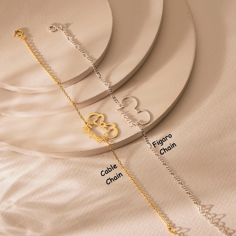 May include: Two personalised bracelets. One gold-coloured bracelet with a Mickey Mouse-shaped charm and the name "Sophia". The other is silver with a Mickey Mouse charm and the name "Lucas". The bracelets are on a neutral background.