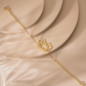 May include: A delicate gold bracelet with a bow-shaped charm and the name "Sophia" in cursive. The fine chain bracelet is displayed on a neutral surface. The bracelet is a stylish piece of jewellery.
