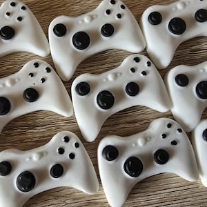 May include: Several white game controller decorations with black buttons and directional pads. The controllers are arranged on a light brown surface, creating a pattern.