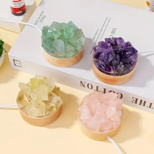 Puede incluir: Cuatro pequeñas lámparas de cristal redondas con bases de madera. Los cristales son verdes, morados, amarillos y rosas. Cada lámpara tiene un cable blanco. Las lámparas están sobre un libro blanco con el texto "THE COTTON".