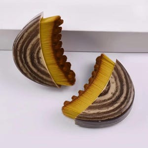 May include: Two halved makeup brushes are shown against a white backdrop. The brushes feature a striped, brown and beige casing with a fan of yellow bristles. The bristles have a dark brown edge.