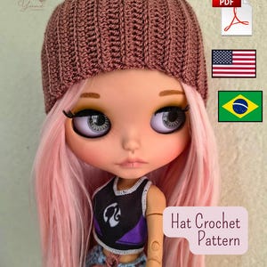 Pode incluir: Uma boneca com cabelo comprido cor-de-rosa usa um gorro de croché canelado de cor malva. A boneca tem olhos grandes e claros e veste um top sem mangas preto e roxo. Uma caixa de texto à direita apresenta as palavras Hat Crochet Pattern.