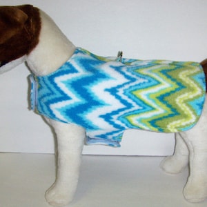 May include: A white, blue, and green chevron patterned dog sweater. The sweater is made of soft fleece and has a comfortable fit.