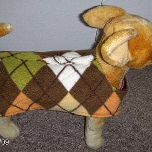 May include: A small brown, tan and green dog sweater with a diamond pattern. The sweater has a loop for a leash.