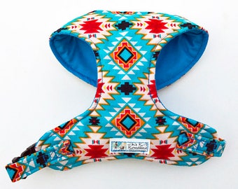May include: A turquoise, red, and white patterned dog harness with a blue lining. The harness has a black buckle and a small label that reads "Janie K's Kreations".