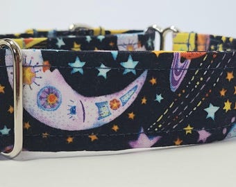 May include: A black dog collar with a celestial design. The fabric features a pattern of stars, planets, and a crescent moon in shades of yellow, blue, purple, and white. The collar has a silver metal buckle.