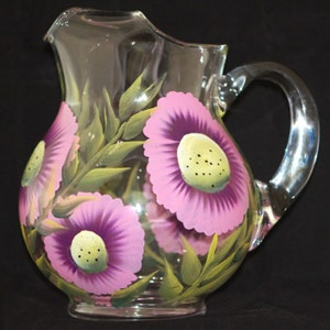 May include: A clear glass pitcher with a painted design of pink and purple flowers with green leaves.