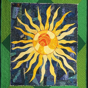 May include: A handmade quilt featuring a vibrant sun design. The sun has yellow and orange rays and a circular center. The background is a mix of blue and green fabrics. The quilt is framed with a green border.