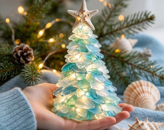 May include: A conical decorative tree sculpture crafted from translucent sea glass pieces in shades of blue, green, and white, illuminated by internal warm lights and topped with a white starfish ornament.