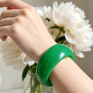 May include: A smooth, solid, vibrant green bangle bracelet with a polished finish. The circular accessory features a wide, rounded band design that maintains a consistent thickness throughout its circumference, showcasing a bright, uniform emerald hue.