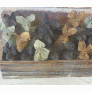 May include: A wooden crate filled with handmade fabric mice. The mice are in various shades of brown, gray, and white. Some of the mice have black eyes and others have white eyes. The mice are all sitting in the crate, looking out at the viewer.
