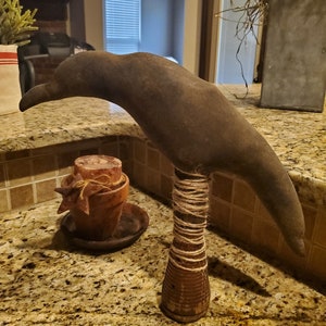May include: A brown, bird-shaped, wooden sculpture with a twine-wrapped base. The sculpture is sitting on a granite countertop.