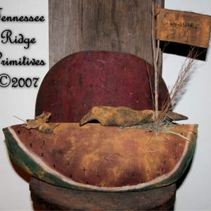 May include: A rustic watermelon-shaped decoration with a red rind and a green edge. A small wooden sign that says "Summer" is attached. The decoration has a vintage, handcrafted appearance, with the text "Tennessee Ridge Primitives ©2007".
