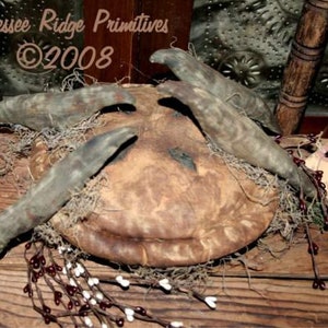 May include: A rustic, handmade pie crust with a brown and tan color, decorated with dried grasses and twigs. The pie crust is surrounded by a garland of white and red berries. The text "Tennessee Ridge Primitives ©2008" is visible in the top left corner of the image.