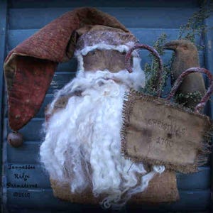 May include: A rustic Santa Claus figure with a long, red hat and a fluffy white beard. A burlap sack with the text "Christmas 1700" is held by a bird-like figure. The figure is set against a blue background. The text "Tennessee Ridge Primitives ©2010" is visible.