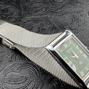 May include: A rectangular Seiko Quartz watch with a silver-tone case and a mesh band. The watch face is green with silver hands and Roman numeral hour markers. The watch is displayed on a textured black surface.
