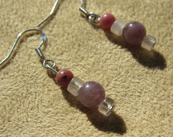 May include: A pair of handmade earrings featuring a combination of pink and purple beads. The earrings have a silver hook and are composed of a small pink bead, a clear cube, a larger purple bead, and a silver spacer.