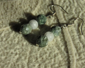 May include: A pair of earrings featuring faceted green and white beads. The earrings have silver-colored fish hook ear wires. The beads are arranged in a circular pattern, with the green beads having a faceted cut.