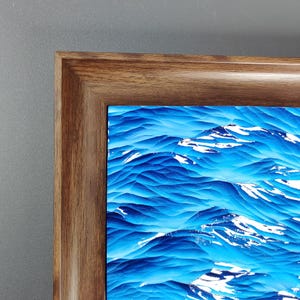 May include: A framed abstract art print featuring a textured, blue and white mountain landscape. The artwork is encased in a dark brown wooden frame, creating a contrast with the vibrant colors of the print.