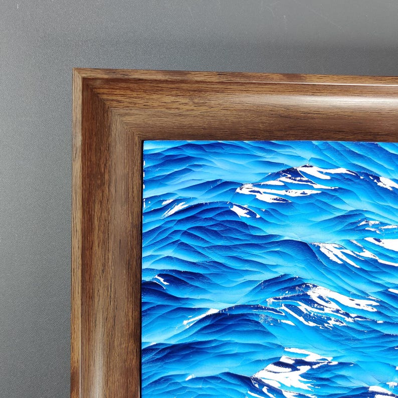 May include: A framed abstract art print featuring a textured, blue and white mountain landscape. The artwork is encased in a dark brown wooden frame, creating a contrast with the vibrant colors of the print.