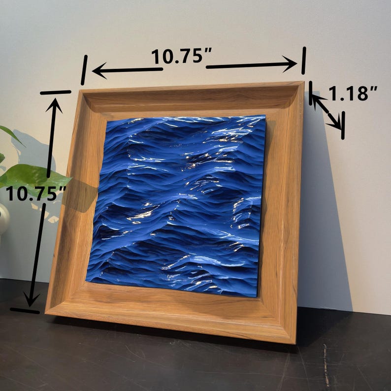 May include: Square wooden frame with a blue wave design, measuring 10.75 inches by 10.75 inches. The frame is 1.18 inches thick, showcasing a textured, ocean-themed artwork. The artwork is a vibrant blue, creating a sense of depth and movement.