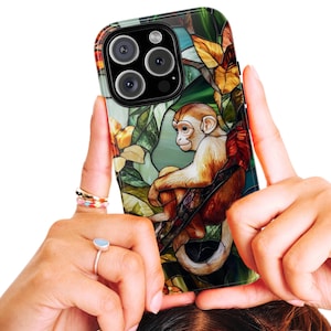 May include: A smartphone case featuring a stained-glass design with a monkey perched on a branch. The case has a colorful floral and foliage background with shades of green, yellow, and red. The monkey is depicted in shades of brown and tan.