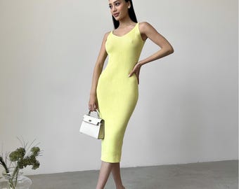 May include: A sleeveless, ribbed knit midi dress in a vibrant yellow color. The dress has a fitted silhouette and a scoop neckline. The model is wearing white strappy sandals and carrying a white handbag. The dress is a stylish choice for warm weather.