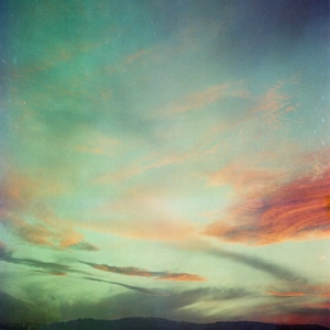 May include: A scenic landscape photograph of a sunset with a gradient of colors. The sky transitions from teal to orange and pink, with wispy clouds and a dark mountain range in the distance.