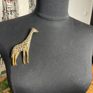 May include: A gold-toned giraffe brooch with clear rhinestones and a single red rhinestone for an eye.