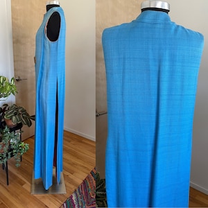 May include: A long, sleeveless, light blue maxi dress with a high neckline and a side slit. The dress is made of a textured fabric.