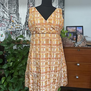 May include: A sleeveless dress with a V-neckline and a checkered pattern in shades of orange, pink, and white.