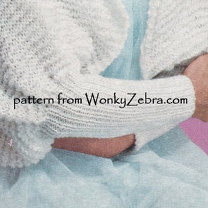 May include: A close-up of a white knitted cardigan with long sleeves. The cardigan is made with a simple stitch pattern and has a relaxed fit. The text "pattern from WonkyZebra.com" is visible on the sleeve.