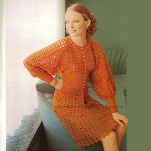 May include: A crocheted dress in a burnt orange color with a fitted bodice and a flared skirt. The dress has a round neckline and long sleeves with a button closure at the front. The dress is made with a delicate openwork stitch.