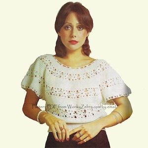 Puede incluir: Una blusa de ganchillo blanca con cuello redondo, mangas cortas acampanadas y bandas horizontales de intrincados patrones calados inspirados en flores. El texto Pattern PDF from WonkyZebra.com by email aparece impreso en el centro.