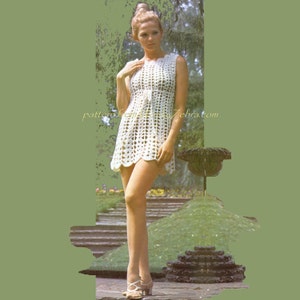 Peut inclure: Une mini-robe sans manches en crochet blanc avec un motif géométrique ajouré, un ourlet festonné et un détail à nouer à la taille. Le texte patternfromvintagezebra.com est visible au centre du vêtement.