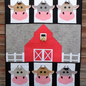 May include: A red barn with white trim and a white picket fence in front. Six cow faces are arranged around the barn, each with a different pattern and color.