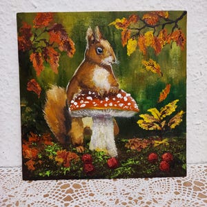 May include: A square painting depicts a brown squirrel perched on a red and white mushroom. The background features autumn leaves in shades of orange and yellow against a green backdrop. Red berries are scattered at the base.